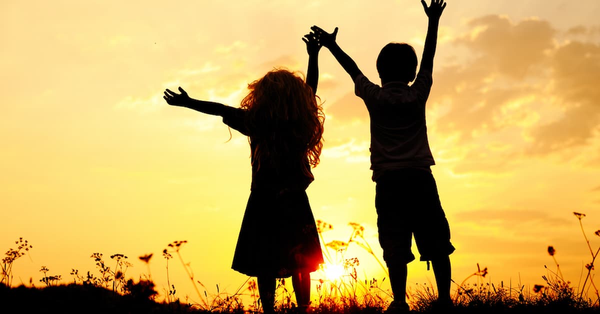 Silhouette, group of happy children playing on meadow, sunset, summertime Children silhouetted against sunset sky.