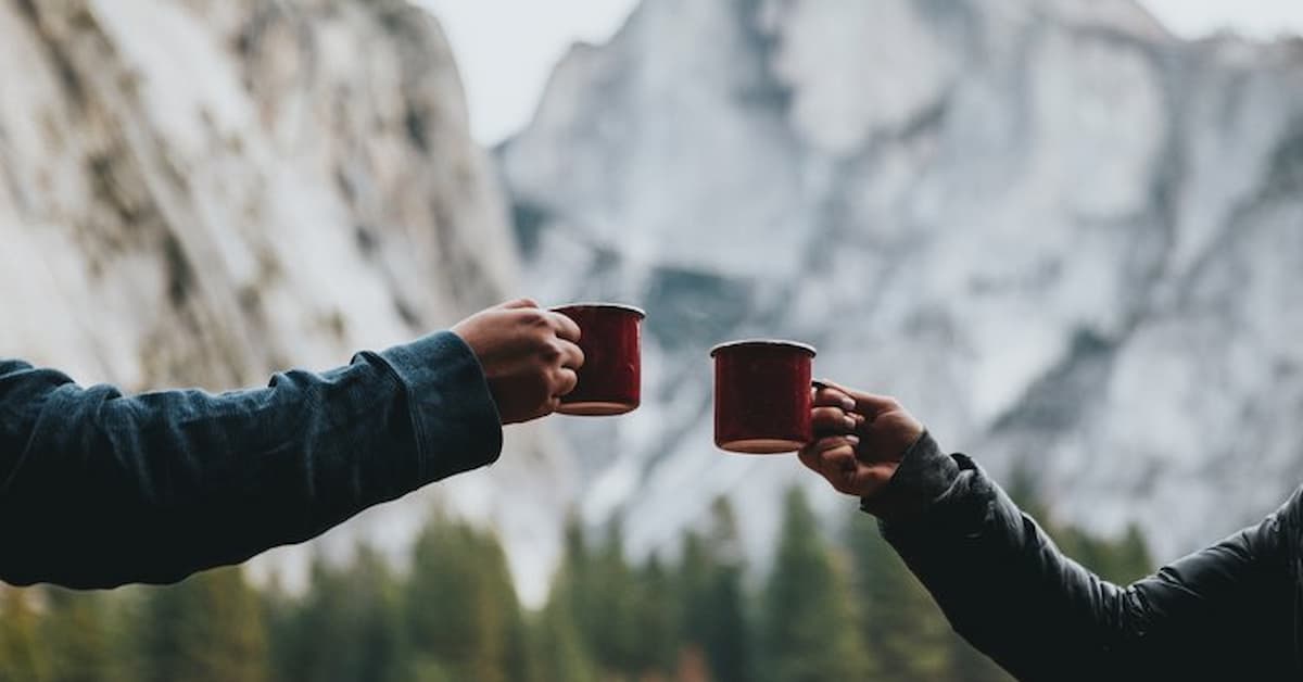 Two hands clinking red mugs outdoors.