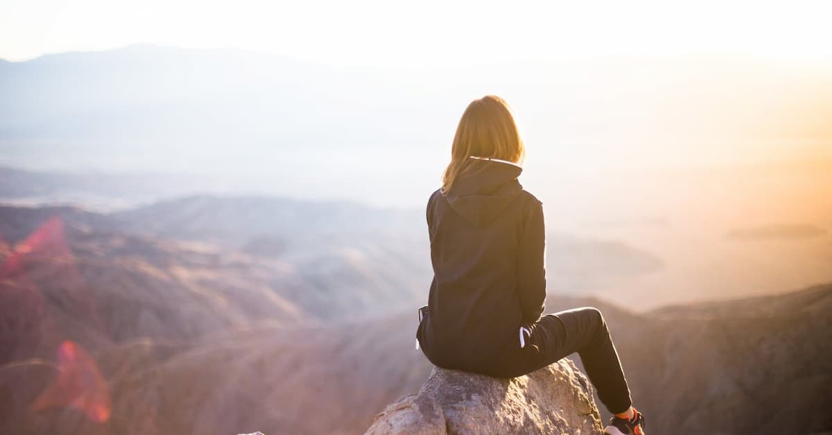 Person sitting on rock, sunset view